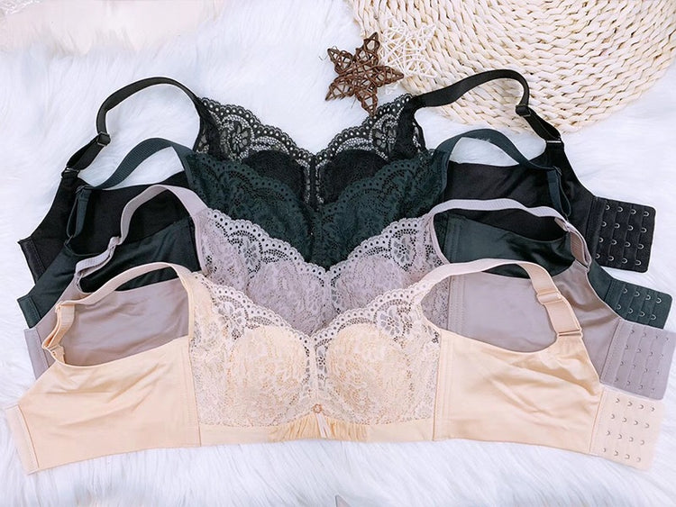 Several bras in pink, beige, black, and green, laid out on a fabric background, showcasing a mix of lace and smooth fabrics.
