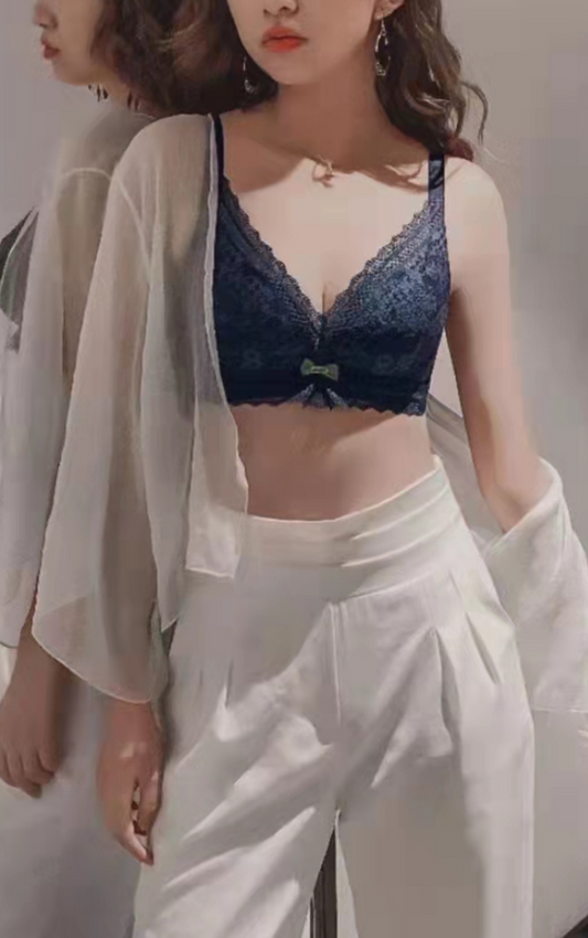 Woman modeling a navy blue wireless bra with a lace overlay, wearing a white outfit.